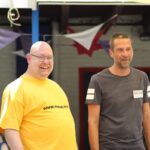 Foto von zwei Männern im Freien beim KiTa RoKoKo Jubiläum, mit bunter Wimpelkette im Hintergrund. Einer trägt Gelb, einer Grau.