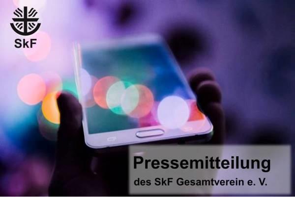 Foto von einer Hand, die ein Smartphone hält; bunte Lichter im Hintergrund. Oben links das SkF-Logo, unten rechts Text: Pressemitteilung des SkF Gesamtverein e. V.