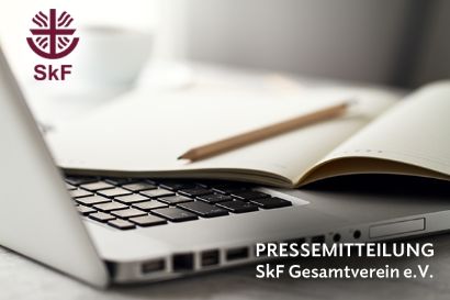 Foto von einem Laptop und einem Notizbuch auf einem Tisch. Beide Gegenstände liegen nebeneinander in einer Arbeitsumgebung.