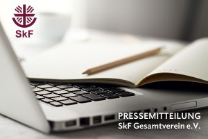 Foto von einer Laptop-Tastatur, darauf ein offenes Notizbuch mit Bleistift. Oben links das SkF-Logo und Text: PRESSEMITTEILUNG SkF Gesamtverein e.V.-aktuelle kirchliche Nachrichten wie aus einer Kirchenzeitung.
