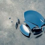 Foto von einem zerbrochenen blauen Teller, dessen große und kleine Scherben auf einer grauen, strukturierten Betonfläche liegen.